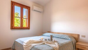 Ein Schlafzimmer mit einem Bett, einem Nachttisch, einem Fenster und einer Klimaanlage.