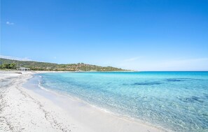 A beach with clear turquoise water, a sandy shore, and a hillside with buildings in the background. - 2 bedroom amazing apartment in Budoni (Budoni)