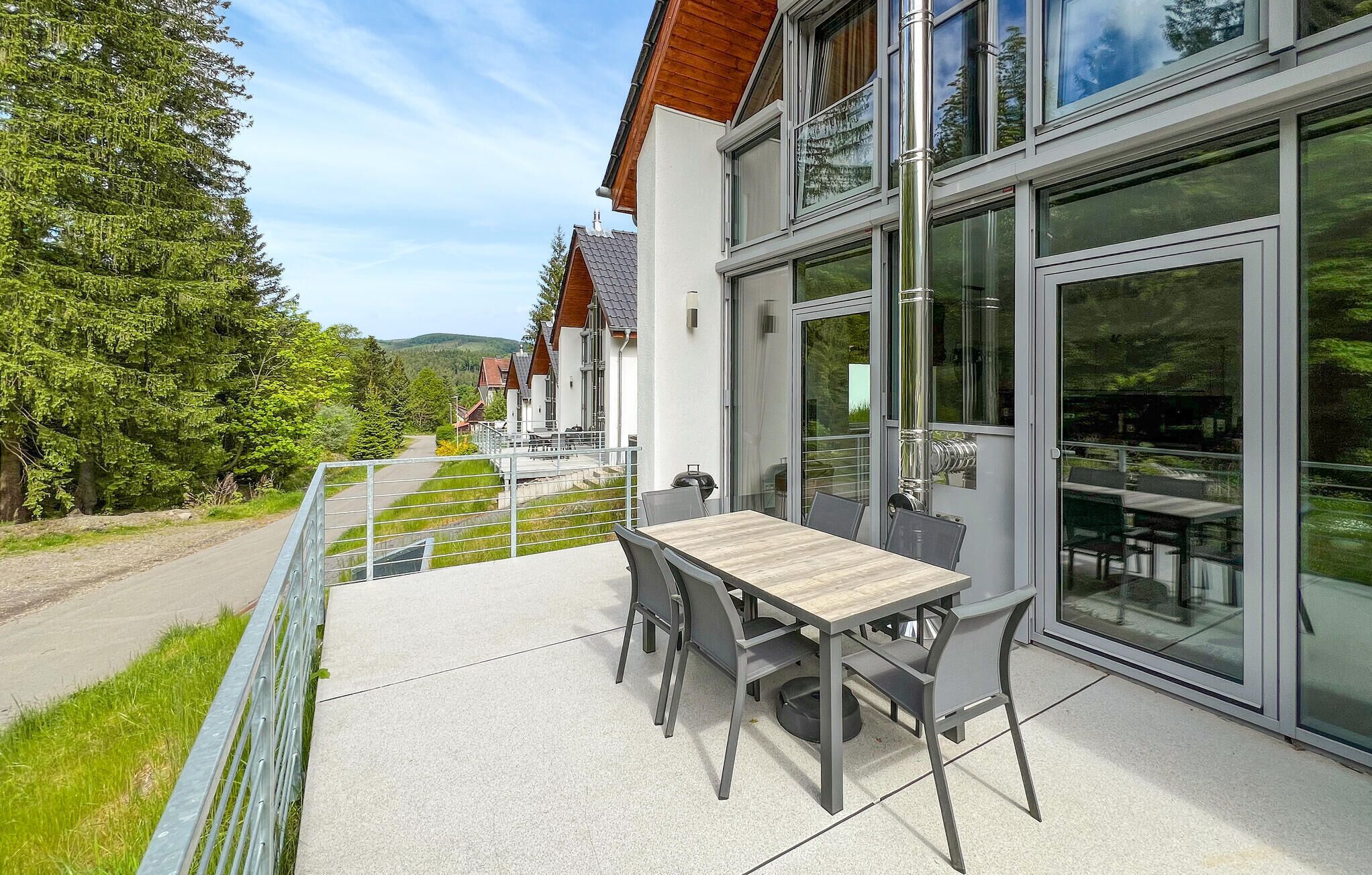 Un bâtiment moderne doté d’un patio avec une table et des chaises, de grandes fenêtres et une vue sur une zone boisée.
