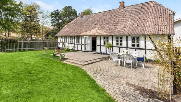 A traditional half-timbered house with a thatched roof, a paved patio with outdoor seating, and a well-maintained lawn. - Cozy home in Dannemare with WiFi (Dannemare)