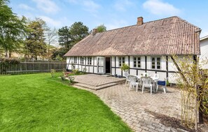 Een traditioneel vakwerkhuis met rieten dak, een geplaveid terras met buitenmeubilair en een verzorgd gazon.