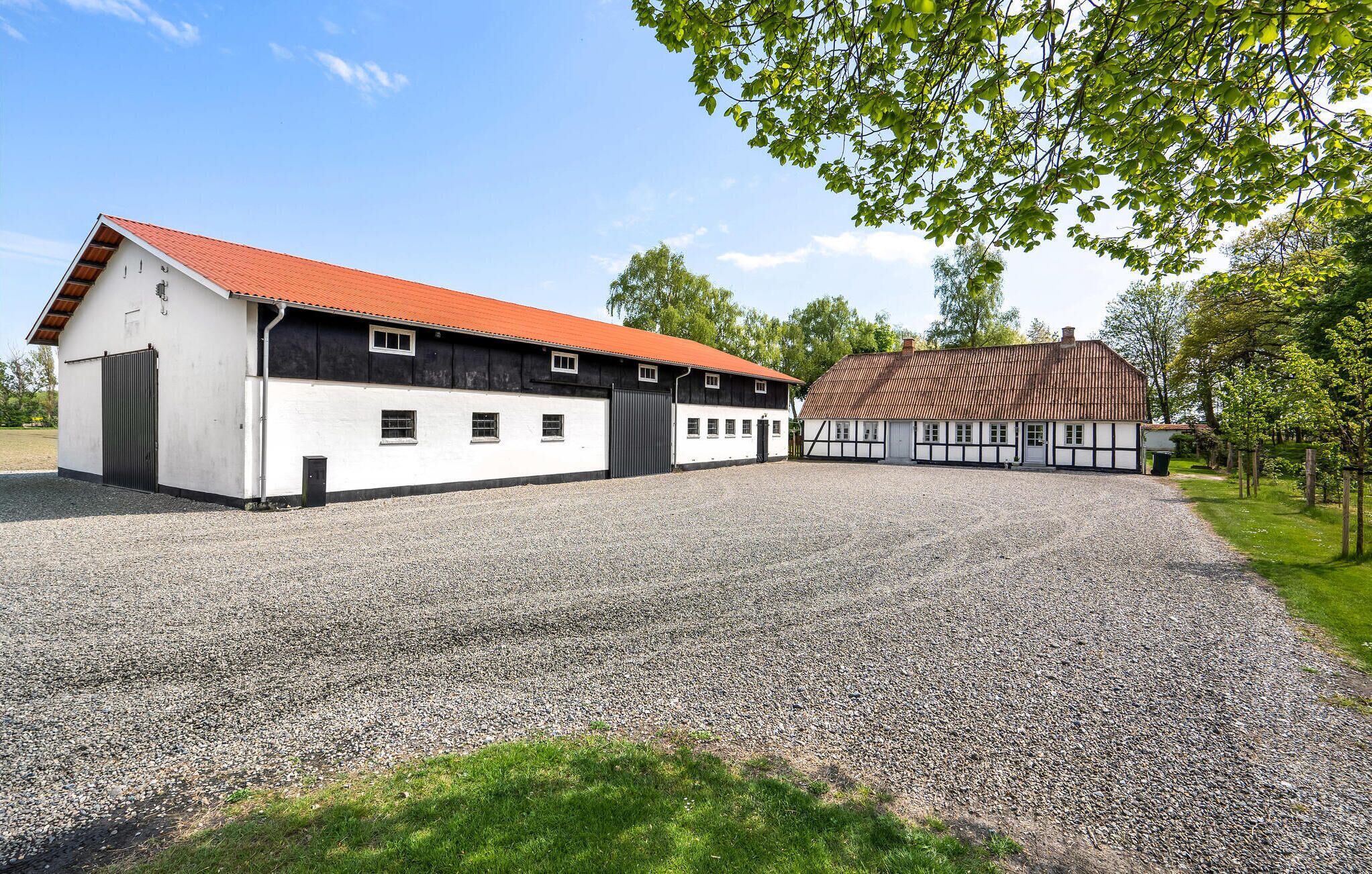 A building with a red roof and white walls, a gravel driveway, and a surrounding grassy area.