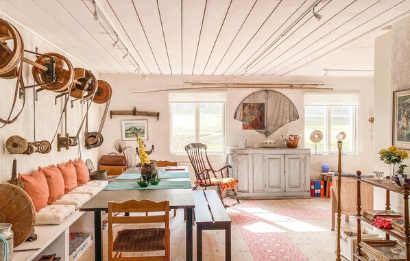 Un coin repas rustique avec une table en bois, des chaises et un canapé. On peut y admirer des jouets anciens à mécanisme sur le mur, un tableau et une fenêtre donnant sur l’extérieur.