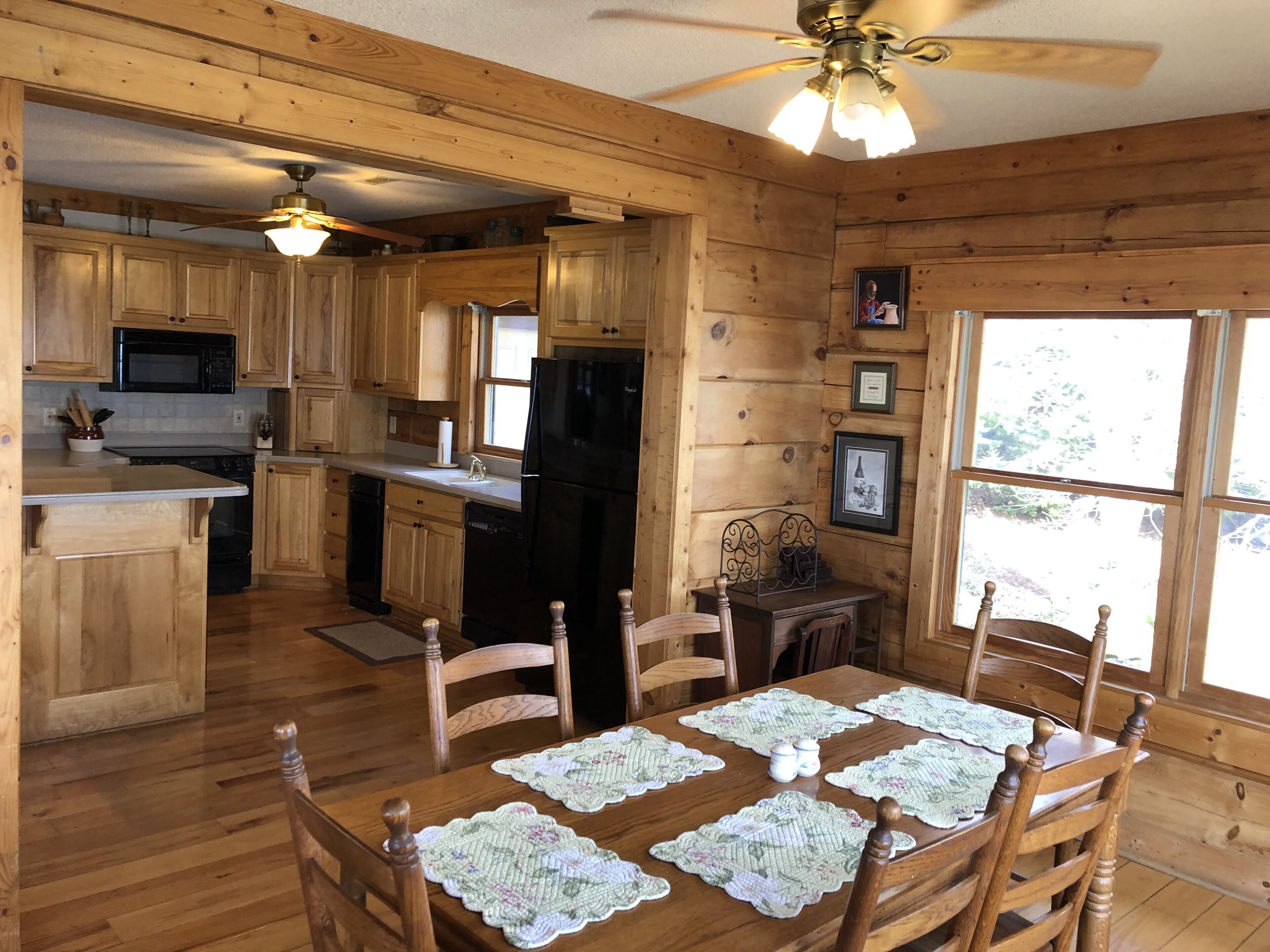 A wooden cabin interior with a kitchen, dining area, and a ceiling fan.