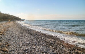 A pebbled beach with a calm sea, a clear sky, and a distant shoreline. - Cozy apartment in Elmenhorst with WiFi (Elmenhorst/Lichtenhagen)