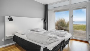 Ein Schlafzimmer mit einem großen Bett, einem Kopfteil, einem Nachttisch und Meerblick durch eine Glastür.