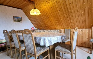 A dining area with a round table and six chairs, wooden walls, and a hanging light fixture. - Cozy apartment in Herrnhut OT Ruppersdor (Herrnhut OT Ruppersdor)