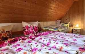 A cozy bedroom with a sloped ceiling, wooden walls, a bed with floral bedding, a teddy bear, and a nightstand with a lamp. - Cozy apartment in Herrnhut OT Ruppersdor (Herrnhut OT Ruppersdor)