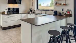 Una cucina moderna con una grande isola, sgabelli da bar e una finestra che offre vista su una casa.
