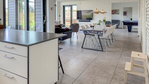 Una cucina moderna con una grande isola, un'area pranzo con tavolo in vetro e un soggiorno con divano e poltrone.