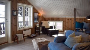 Een knus loft-woonkamer met houten wanden, een blauwe bank, een pluizig voetenbankje en een aan de muur bevestigde televisie.