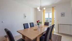 Un comedor con una mesa de madera, sillas negras, un florero con flores y vista al exterior a través de una ventana con cortinas amarillas.