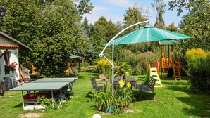 Un jardin avec une table de ping-pong, des chaises, une table ornée d’une plante, un ballon de foot et une balançoire.