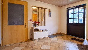 Un couloir avec une porte en bois, une armoire blanche, un miroir et une fenêtre donnant sur des arbres.