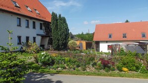 Il s’agit d’un quartier résidentiel composé de deux maisons : l’une a un toit rouge et l’autre une façade blanche. On aperçoit une clôture en bois au premier plan et une route au milieu du paysage.