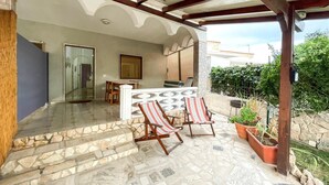 A covered patio area with stone flooring, two striped lounge chairs, a small table, and a bar area with a television. - Lovely home in Marina di Lizzano with WiFi (Marina di Lizzano)