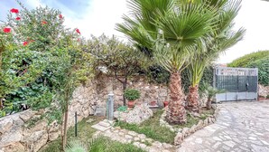 A garden with a palm tree, red flowers, and a stone wall. - Lovely home in Marina di Lizzano with WiFi (Marina di Lizzano)