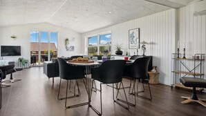 Un vaste espace dédié à la salle à manger, doté d’un haut plafond, de grandes fenêtres et offrant une vue sur l’extérieur. On y trouve plusieurs tables à manger avec des chaises, un téléviseur et des objets décoratifs.