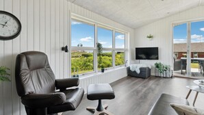Un salon moderne avec un fauteuil en cuir, un pouf gris et un téléviseur à écran plat.