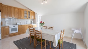 A compact kitchen with wooden cabinets, a dining table with chairs, and a white chair. - Nice apartment in Podstrana with WiFi (Podstrana)