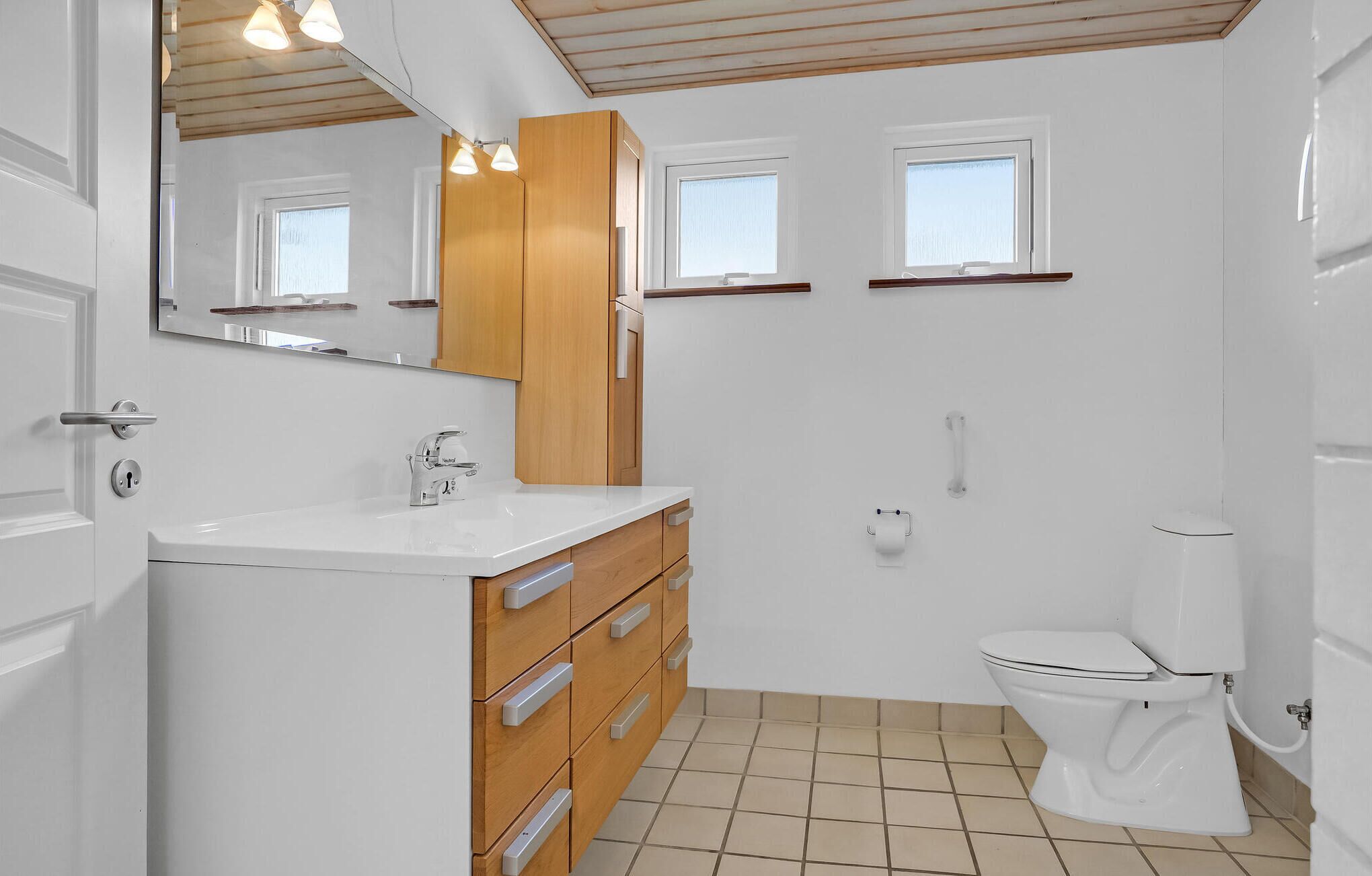 Une salle de bain moderne avec un lavabo blanc, des meubles en bois, des toilettes et un miroir au-dessus du lavabo.