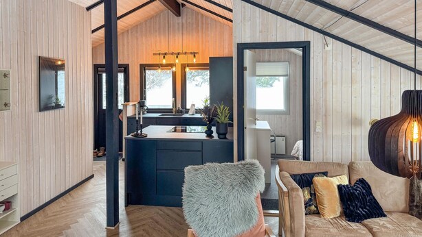 Une cuisine moderne dotée d’un îlot central, de murs en bois et d’un coin salon confortable avec un canapé et un fauteuil.