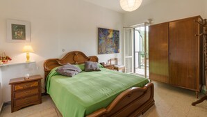 A bedroom with a wooden bed, a nightstand, a lamp, a wardrobe, and a painting on the wall.