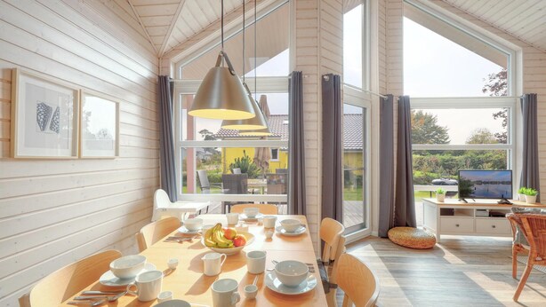A dining area with a wooden table set for four, surrounded by chairs. There are framed pictures on the wall, a large window with curtains, and a television on a stand in the background. - Cozy home in Krems II/Warderbrück with sauna (Krems II/Warderbrück)
