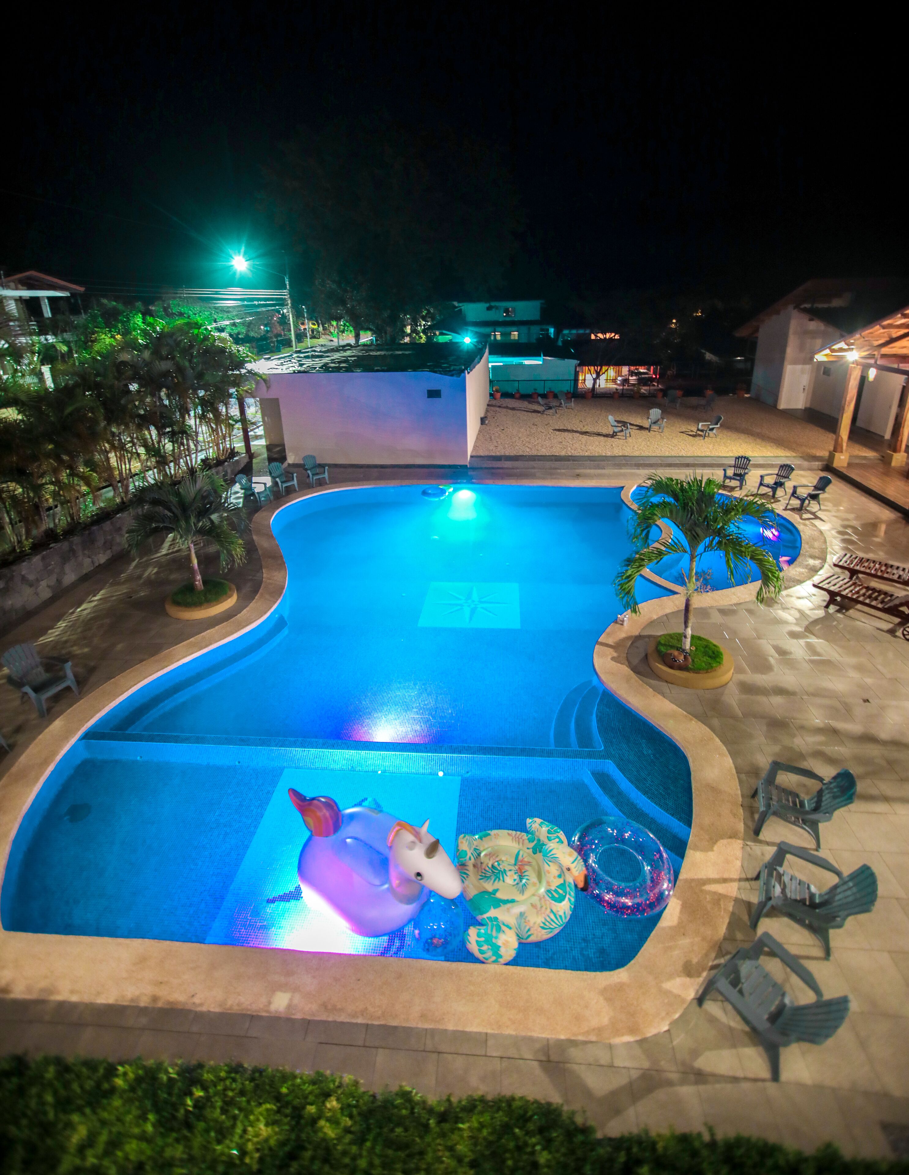Piscina com boia de unicórnio, cercada por espreguiçadeiras e palmeiras.