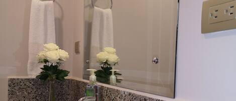 A bathroom with a white sink, a mirror, and a vase with pink flowers on the countertop.