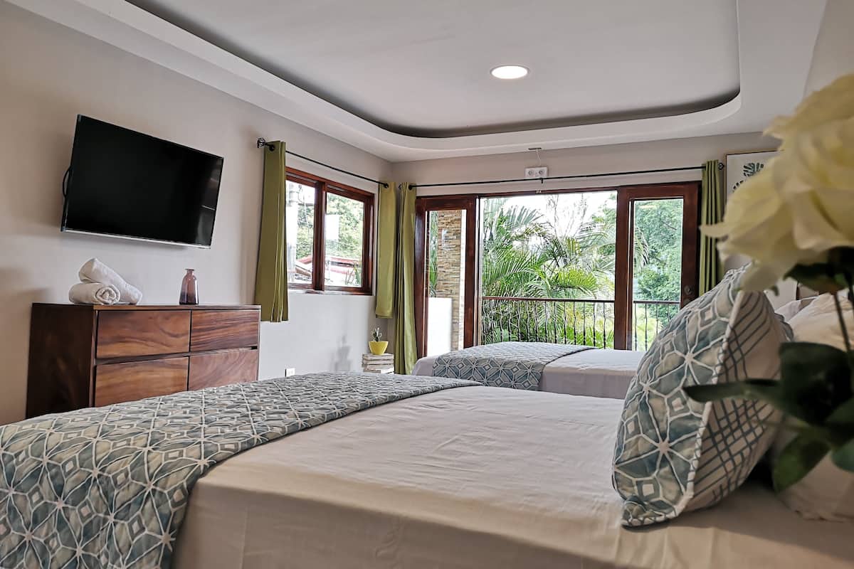 A bedroom with a bed, a TV mounted on the wall, and a window with curtains.