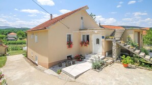 A two-story house with a red-tiled roof, a stone staircase, and a small garden area with potted plants. - Amazing home in Suhac (Suhac)