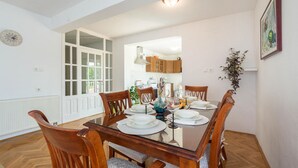 A dining area with a glass table, wooden chairs, and a white wall with a clock and a framed picture. - Amazing home in Suhac (Suhac)