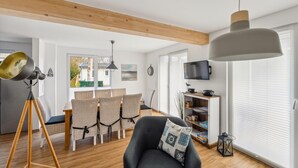 A modern living room with a dining area, wooden beams, a large pendant light, and a television. - Beautiful home in Süssau/Ostsee with sauna (Süssau/Ostsee)