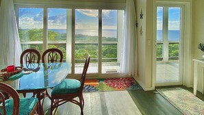 A dining area with a glass table, wooden chairs, and a view of the outdoors through large windows. - Luxury Ocean View Villa in West Bay Roatan. 3 Bedrooms with Pool & Beach Access (Roatan)