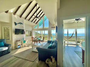A spacious living room with a large window overlooking a scenic view, a ceiling fan, and a dining area with chairs and a table. - Luxury Ocean View Villa in West Bay Roatan. 3 Bedrooms with Pool & Beach Access (Roatan)