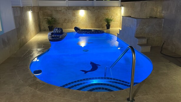 An indoor swimming pool with a blue floor, a diving board, and a staircase leading to a higher level. - Vamos a la playa, private pool/central AC (Vega Alta)