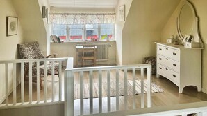 Een kamer met een ledikantje, een dressoir, een radiator en een raam met gordijnen.