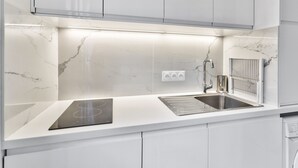 A modern kitchen with white cabinetry, a built-in stove, a stainless steel sink, and a microwave. - Studio Tempa, proche du Château de Vincennes - Welkeys (Vincennes)