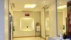 Zona de recepción de hotel con un reloj digital, una planta en maceta pequeña y un mostrador de recepción con un dispensador de gel antibacterial.