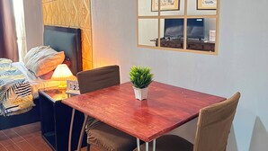 Una habitación acogedora con una mesa de madera, dos sillas, una planta pequeña en maceta, una cama con cabecera y una pared decorada con marcos de fotos.