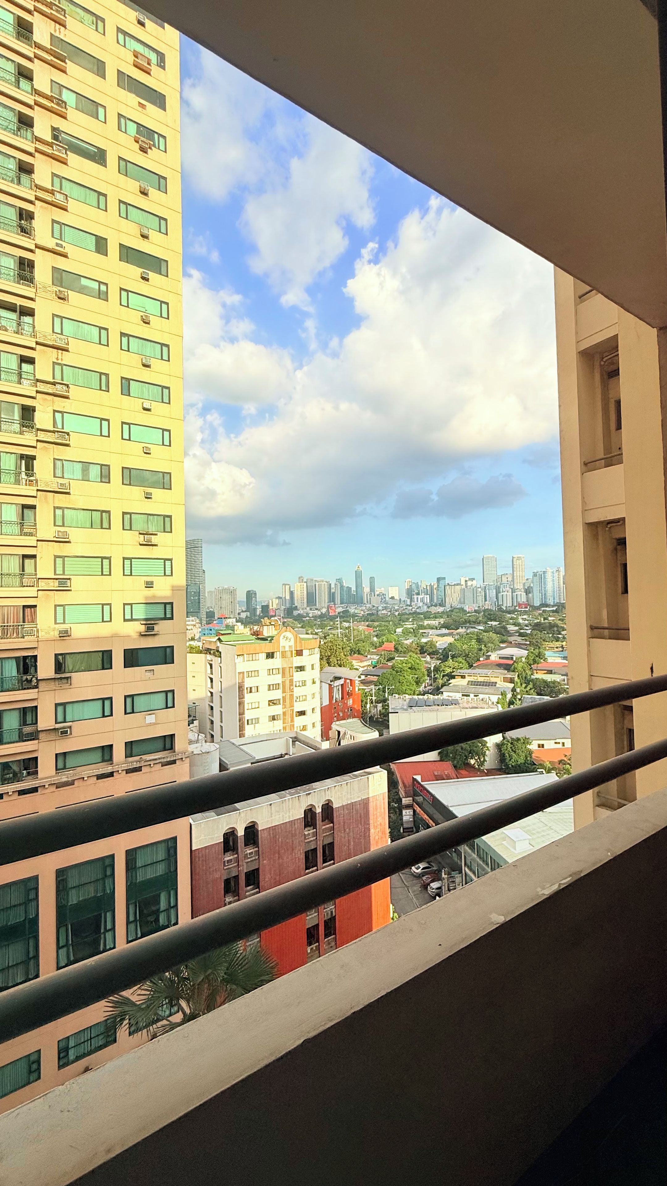 A high-rise building with multiple floors and balconies, a clear sky with clouds, and a distant city skyline.