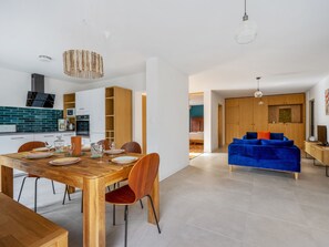 Ein zeitgemäßer Wohnraum mit einem Holzesstisch, Stühlen, einem blauen Sofa und einer Küchenzeile mit Fliesenrückwand und Holdekor-Schränken.