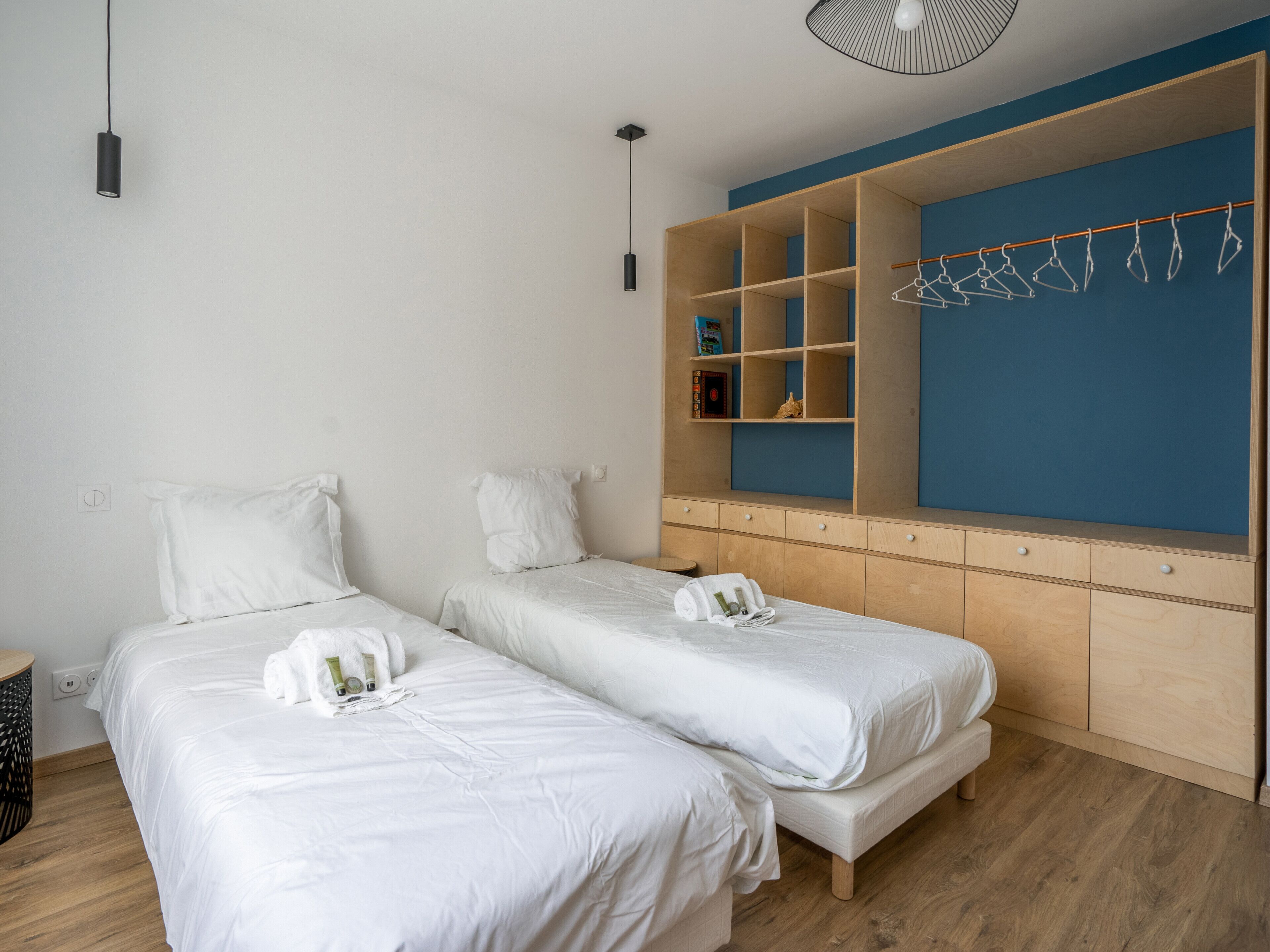 A hotel room with two single beds, a wooden wardrobe, and a blue accent wall.