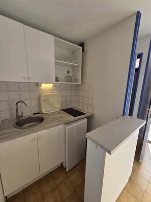 Uma cozinha compacta com armários brancos, lava-louças embutida, pia e bancada com uma chaleira.
