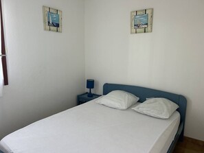 A single bed with white bedding, a blue headboard, and two wall-mounted paintings.