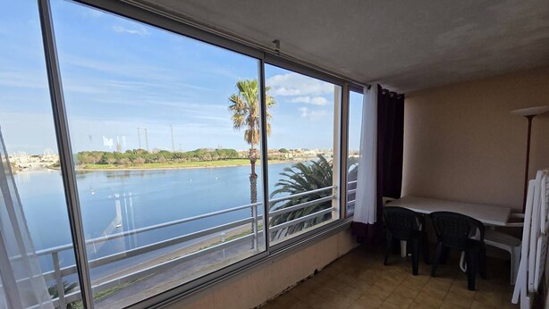 A balcony with a view of a body of water, palm trees, and distant buildings. - 2 Room apartment with pool Richelieu beach Cap d'Agde (LE CAP D AGDE)