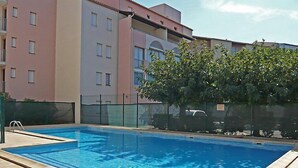 A rectangular swimming pool with a tiled deck, surrounded by a fence and a building with multiple windows and balconies. - 2 Room apartment with pool Richelieu beach Cap d'Agde (LE CAP D AGDE)