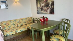 A dining area with a green table and matching chairs, a floral sofa, and a wall-mounted lamp. - 2 Room apartment with pool Richelieu beach Cap d'Agde (LE CAP D AGDE)