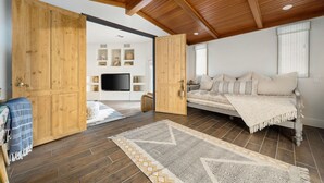 Amplia habitación con una gran puerta de madera, una cama con muchas almohadas, un televisor y una alfombra estampada.